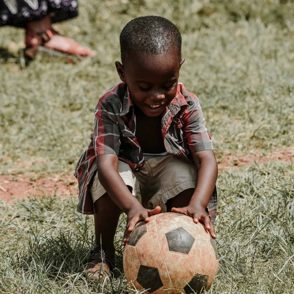 A very young black boy happily smiling and getting ready to kick a football