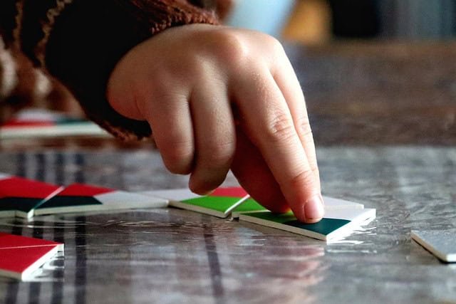 close up of the fingers of a toddler moving a piece of a jigsaw puzzle